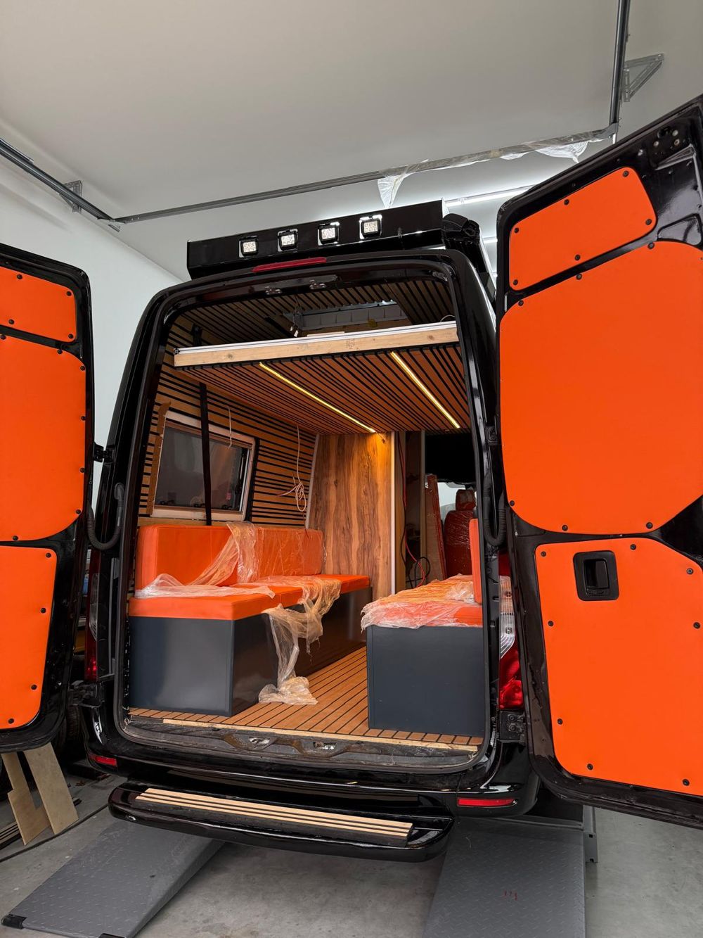 Interieur van een omgebouwde camper: lattenwanden, LED en oranje banken